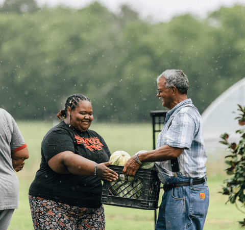 A farmer handing a crate of vegetables to another person.